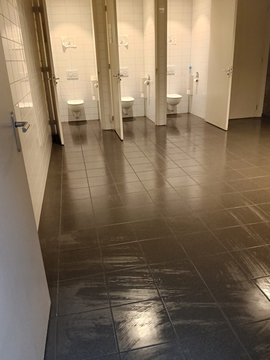 Toiletgroep met drie hokjes en een glanzend schoongemaakte tegelvloer