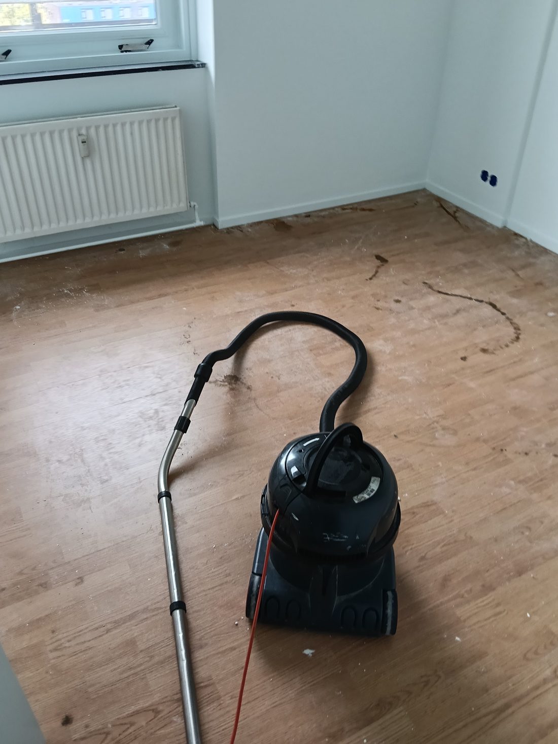 Stofzuiger op een houten vloer vol plamuurresten en krassen na een verbouwing